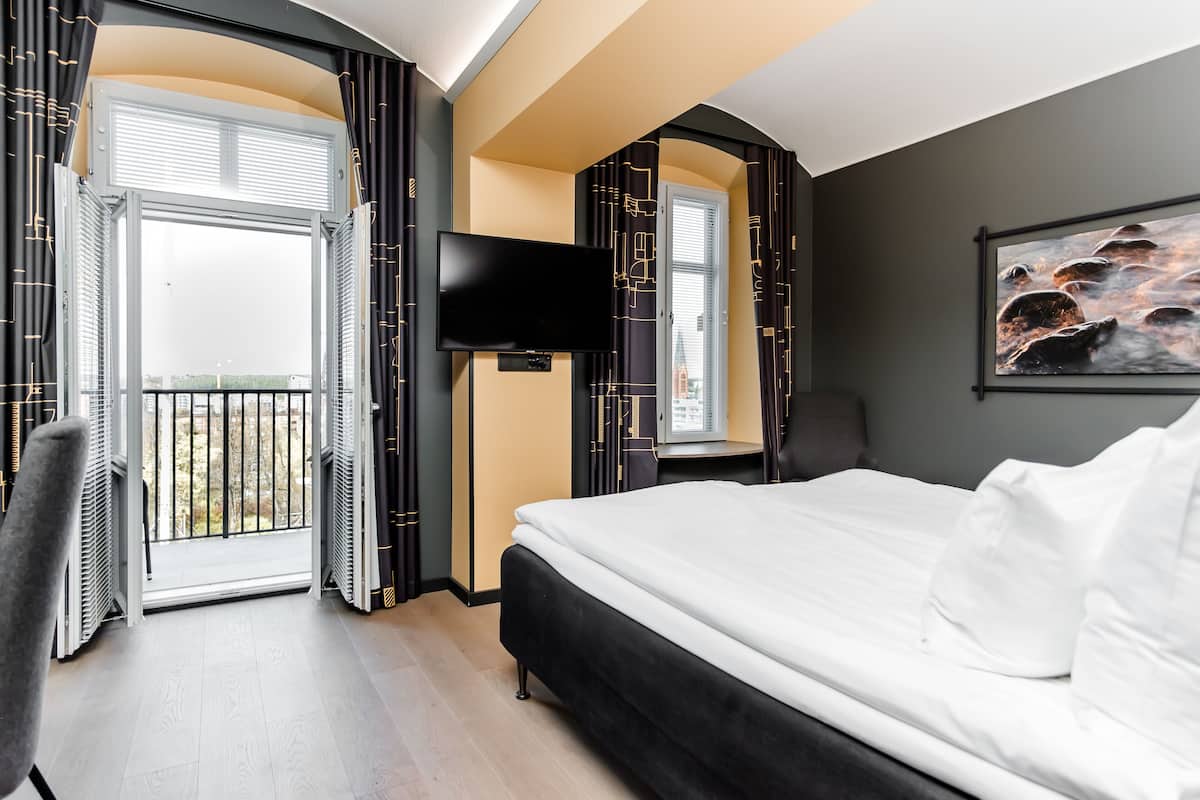 A hotel room with a bed, a TV, a painting, and a balcony with curtains.