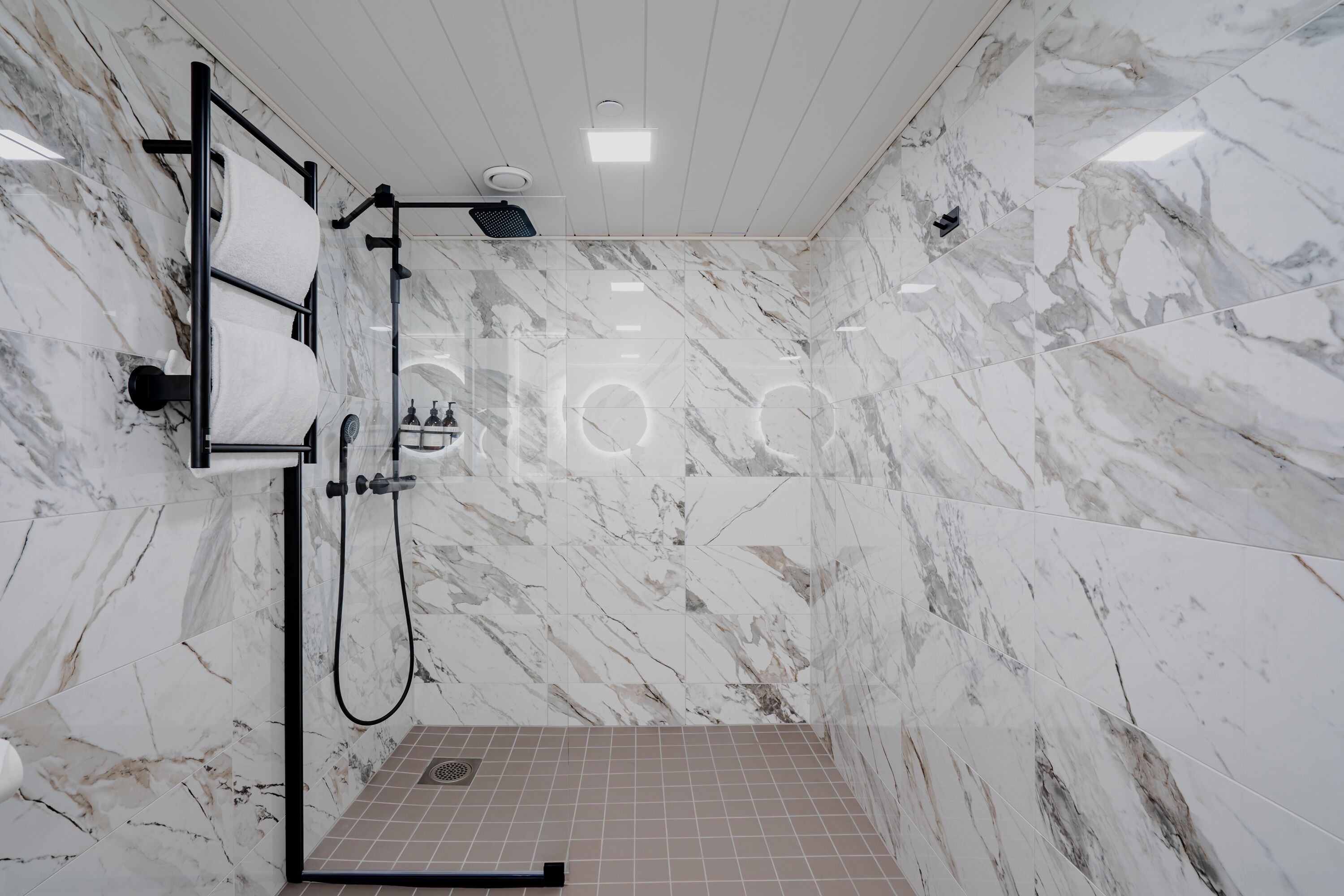 Un baño moderno con paredes y suelo de mármol, un toallero empotrado y una zona de ducha.