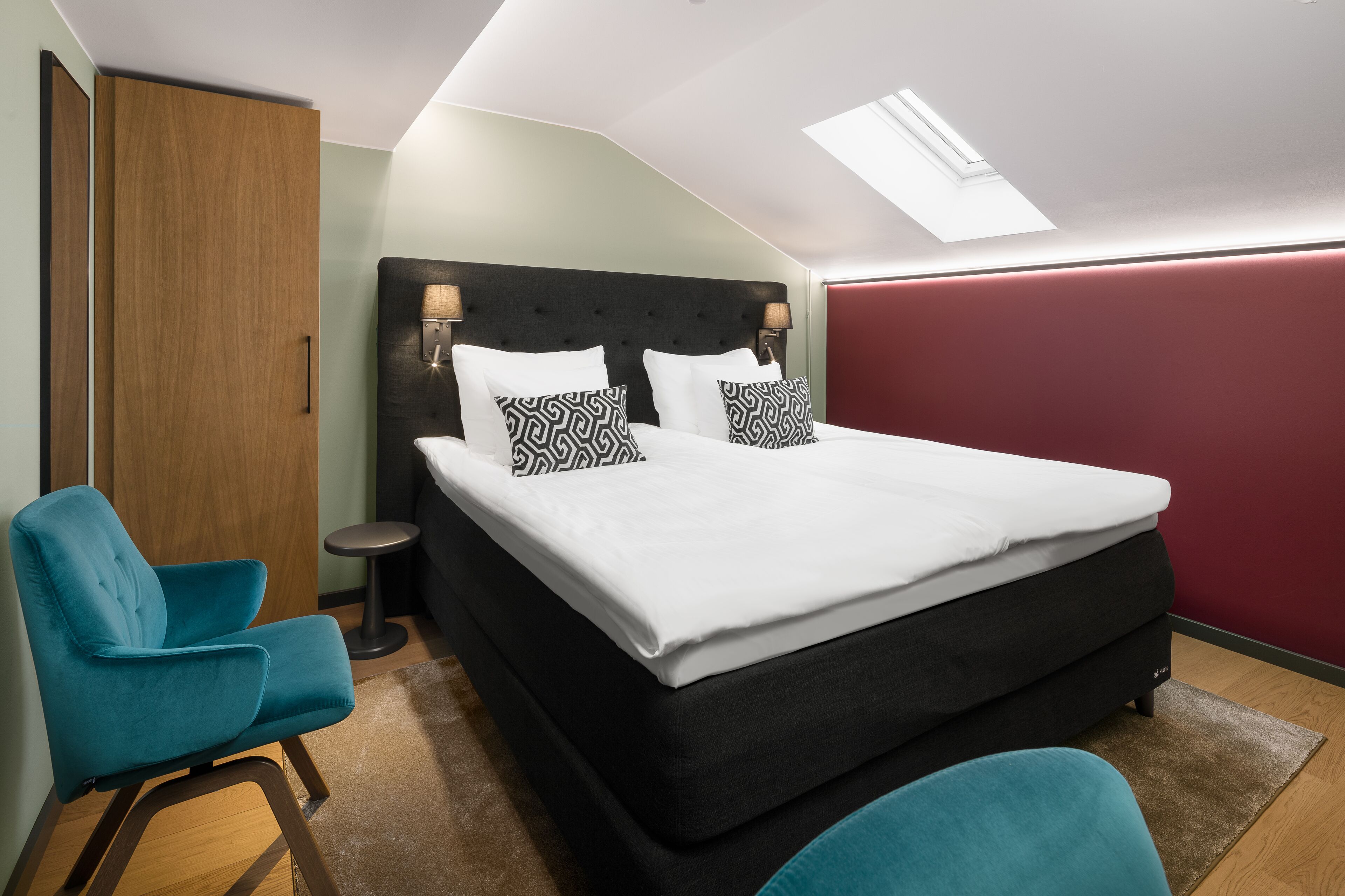 A bedroom with a bed, two chairs, a bedside table, and a skylight.