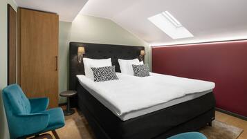 A bedroom with a bed, two chairs, a bedside table, and a skylight.