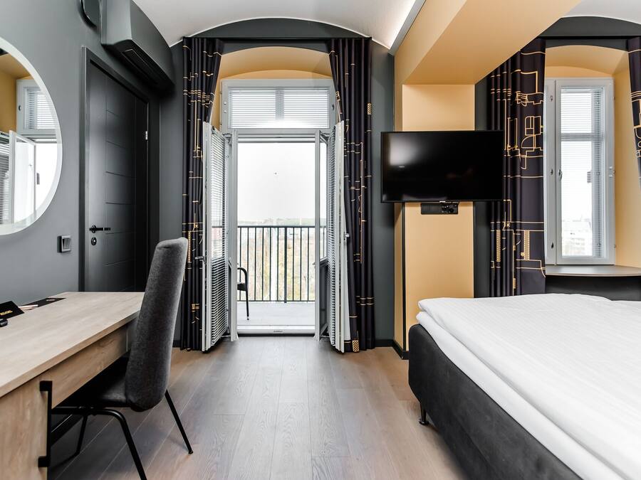 Une chambre d’hôtel avec un lit, un bureau, une chaise, une télévision et un balcon avec des rideaux.
