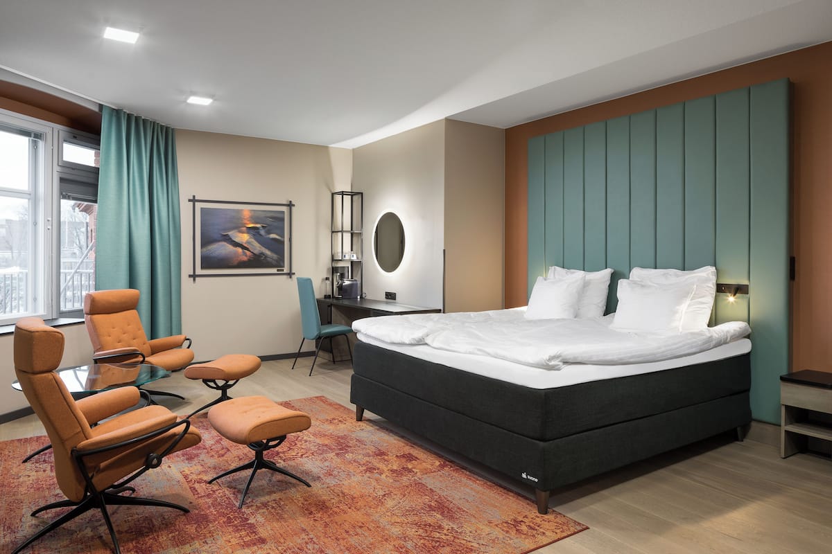 A modern hotel room with a large bed, a desk, and two armchairs.