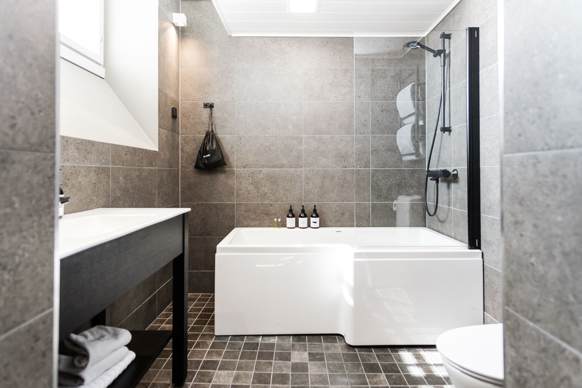 Un baño moderno con bañera, ducha e inodoro. Hay un perchero con toallas y un bolso colgado en la pared.