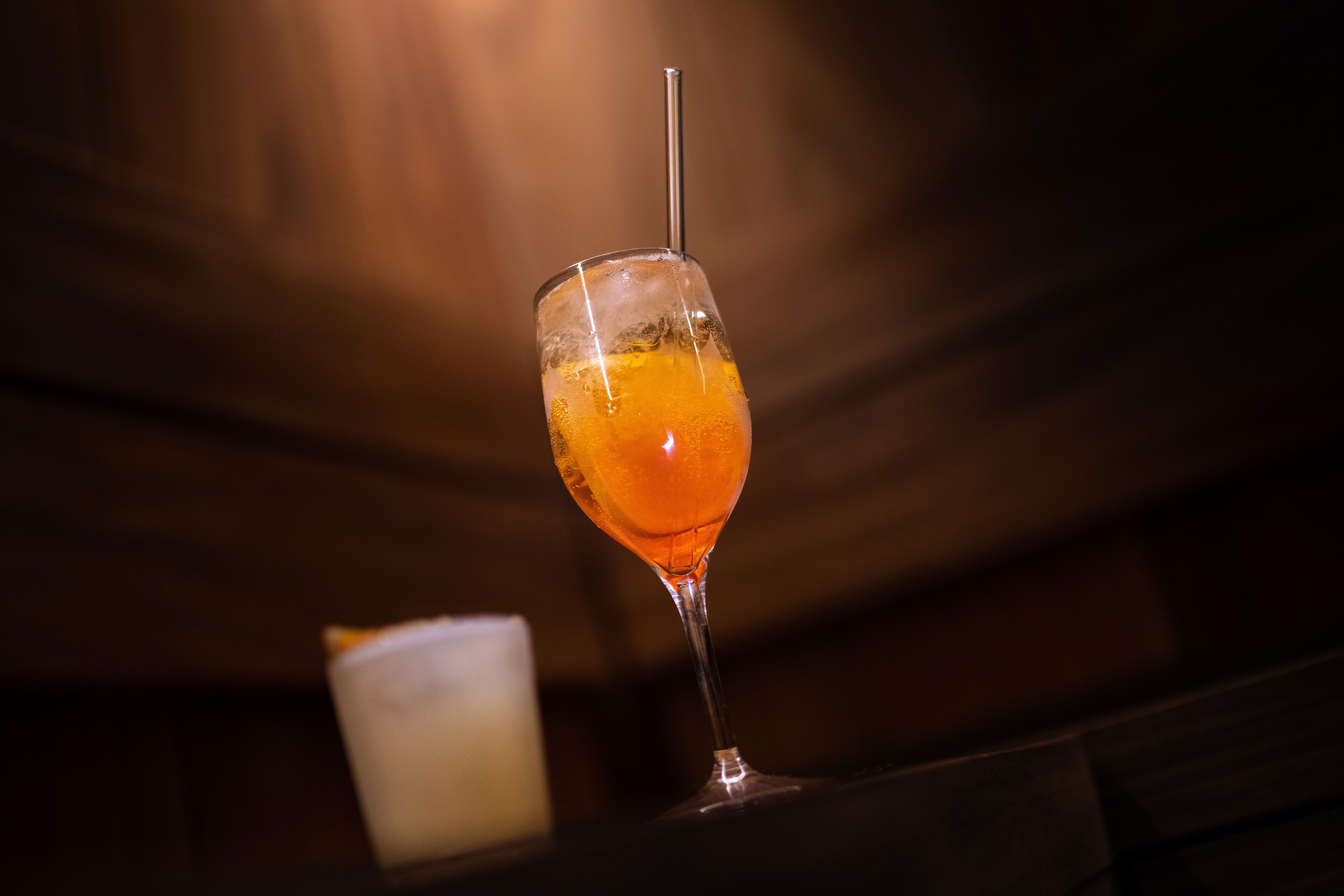 A glass of orange-colored drink with a straw, placed on a wooden surface.