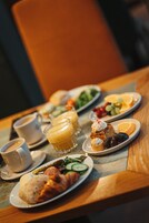 Una mesa de desayuno con diversos platos, como cruasanes, fruta y bebidas.