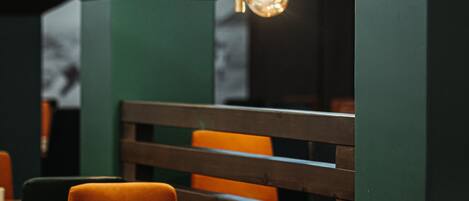 A restaurant interior with a wooden table, orange chairs, and a hanging light fixture with spherical elements.