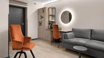 Un salon moderne avec un canapé gris, des fauteuils orange, une petite table ronde, un meuble en bois avec un miroir et une machine à café.