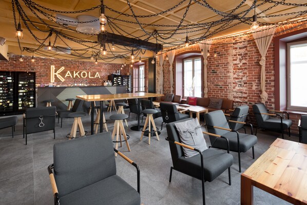 A modern bar area with exposed brick walls, a wooden bar counter, and multiple seating options including bar stools and chairs. - Hotel Kakola (Turku)
