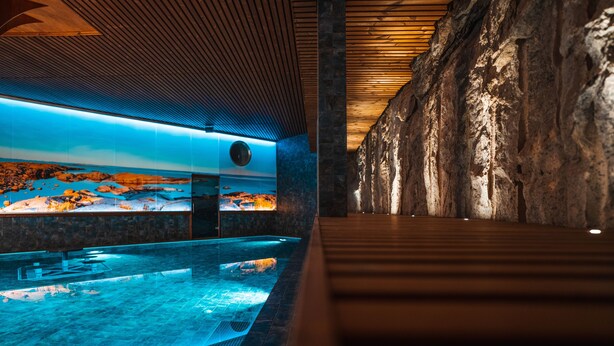 A modern indoor swimming pool with a wooden ceiling and a large rock wall. - Hotel Kakola (Turku)