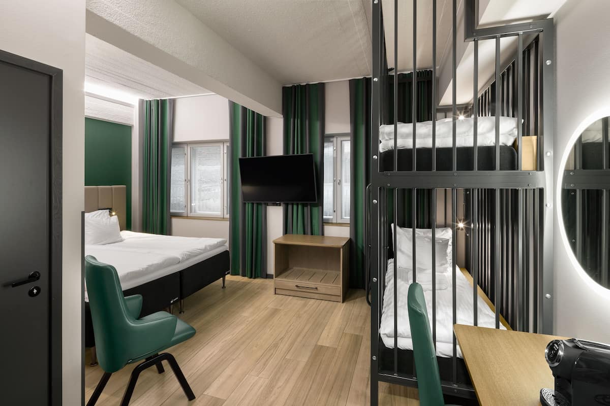 A hotel room with bunk beds, a desk, a chair, a TV, and a window with curtains.