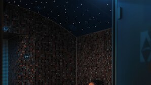 A woman sitting on a tiled bench in a room with mosaic walls and a starry ceiling. - Hotel Kakola (Turku)
