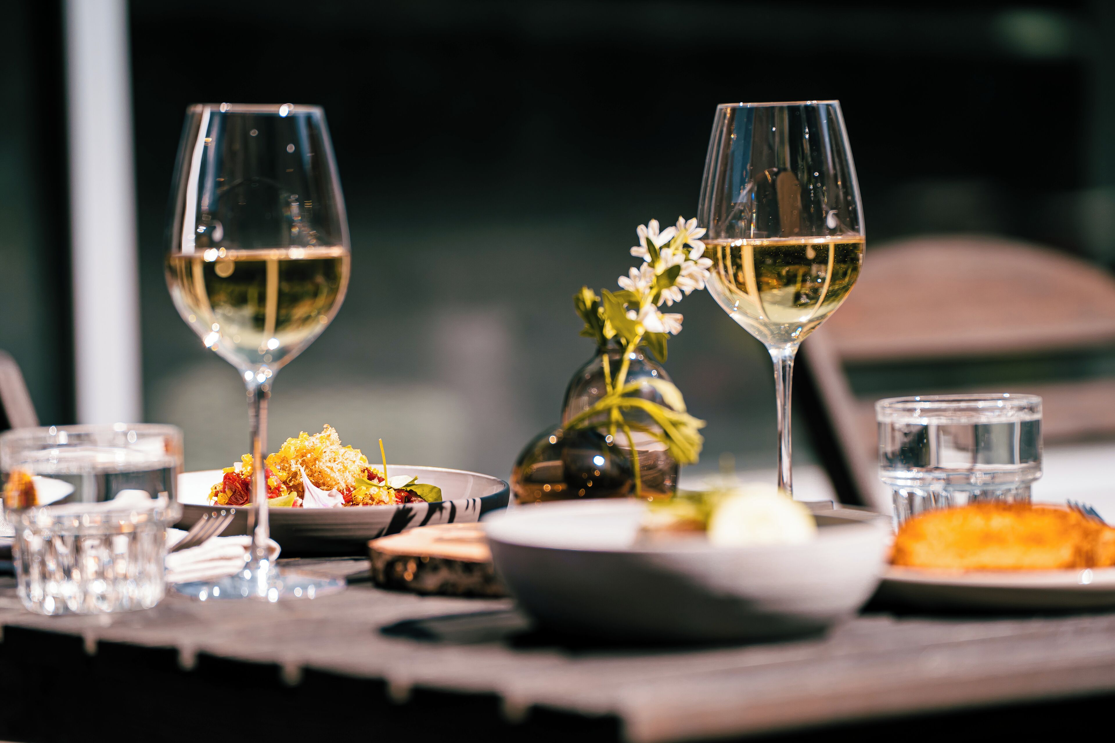 A dining table with two wine glasses, a vase with flowers, and various dishes.