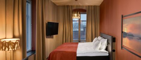 Una habitación de hotel con cama, televisión, ventana con cortinas, lámpara y un cuadro en la pared.