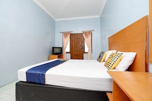 A bedroom with a bed, a wooden headboard, a nightstand, a television, and curtains. - OYO 2240 Simpang Tujuh Residence (Kudus)