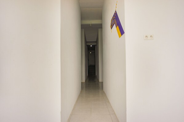 A narrow, well-lit hallway with white walls and a tiled floor, leading to a darker room at the end.