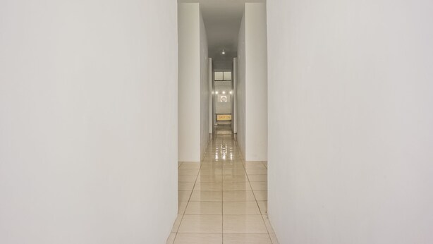 A long, narrow hallway with white walls and a tiled floor, leading to a room with a window and a sign that reads "SPOT ON". - OYO 2277 Lulu Homes (Makassar)