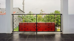 A balcony with a geometric metal gate and red brick wall, overlooking a residential area with greenery and a tall communication tower. - OYO 2277 Lulu Homes (Makassar)