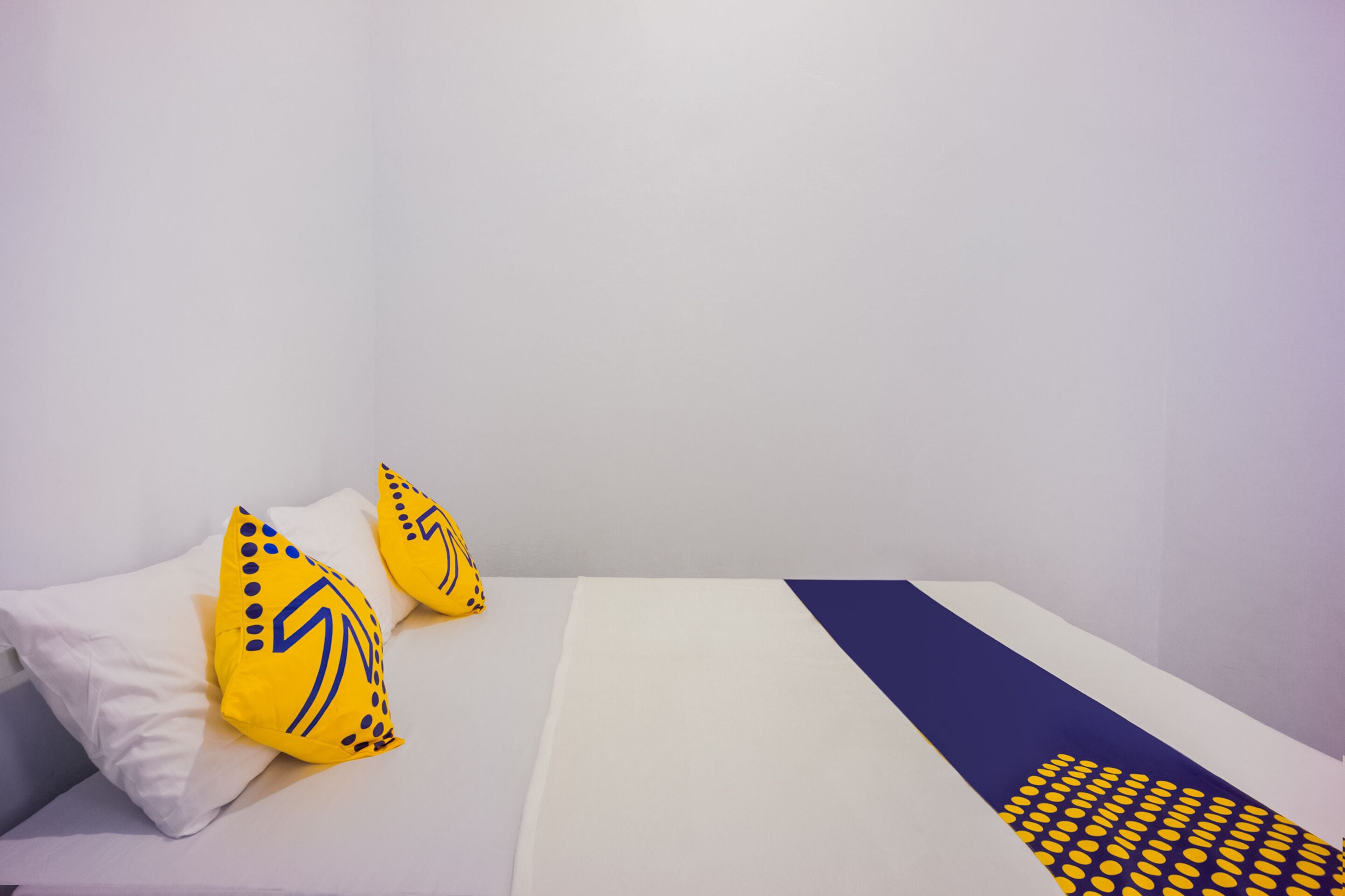 A bed with white bedding, two yellow pillows with a blue pattern, and a blue and yellow blanket.