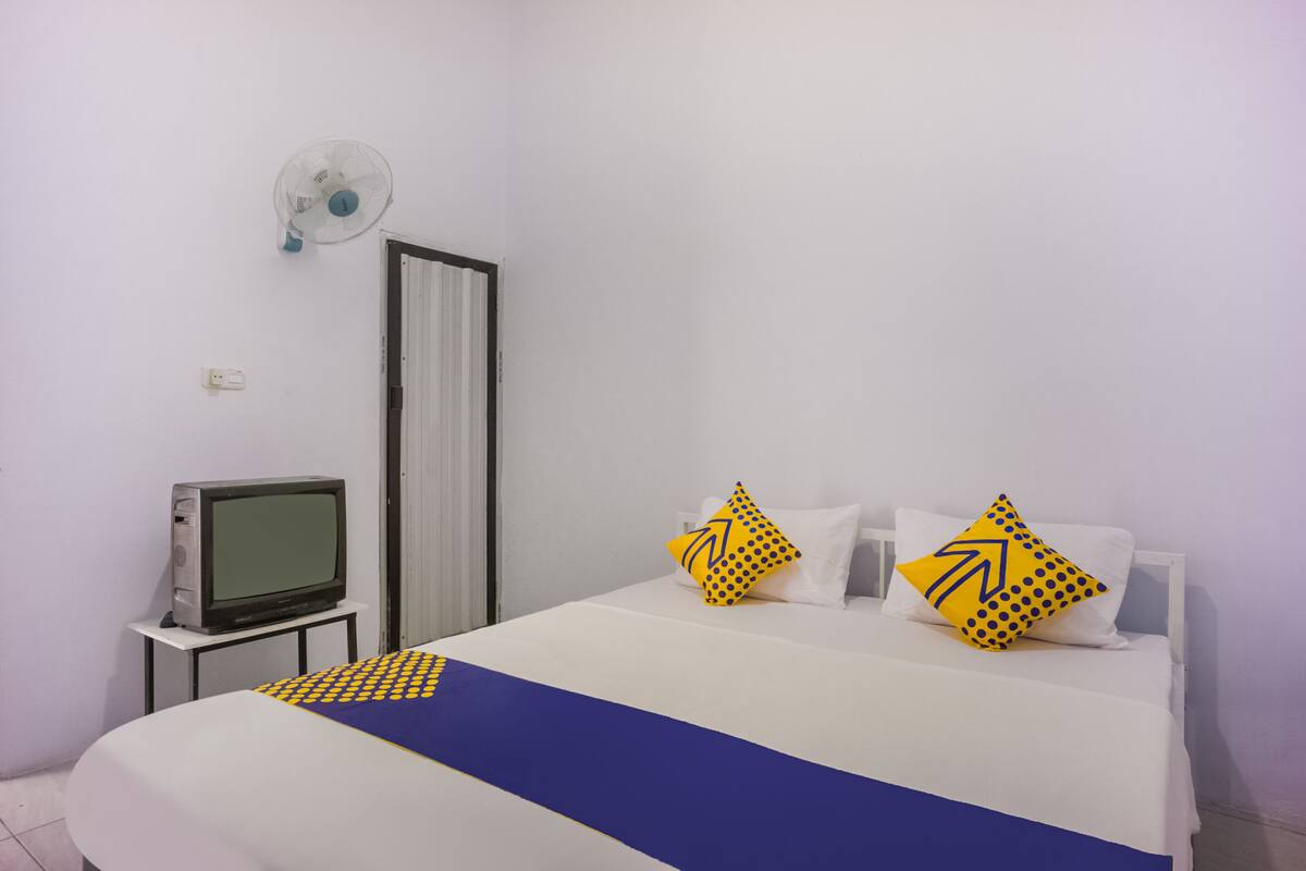 Habitación de hotel con cama, televisión sobre una mesita y ventilador de pared.
