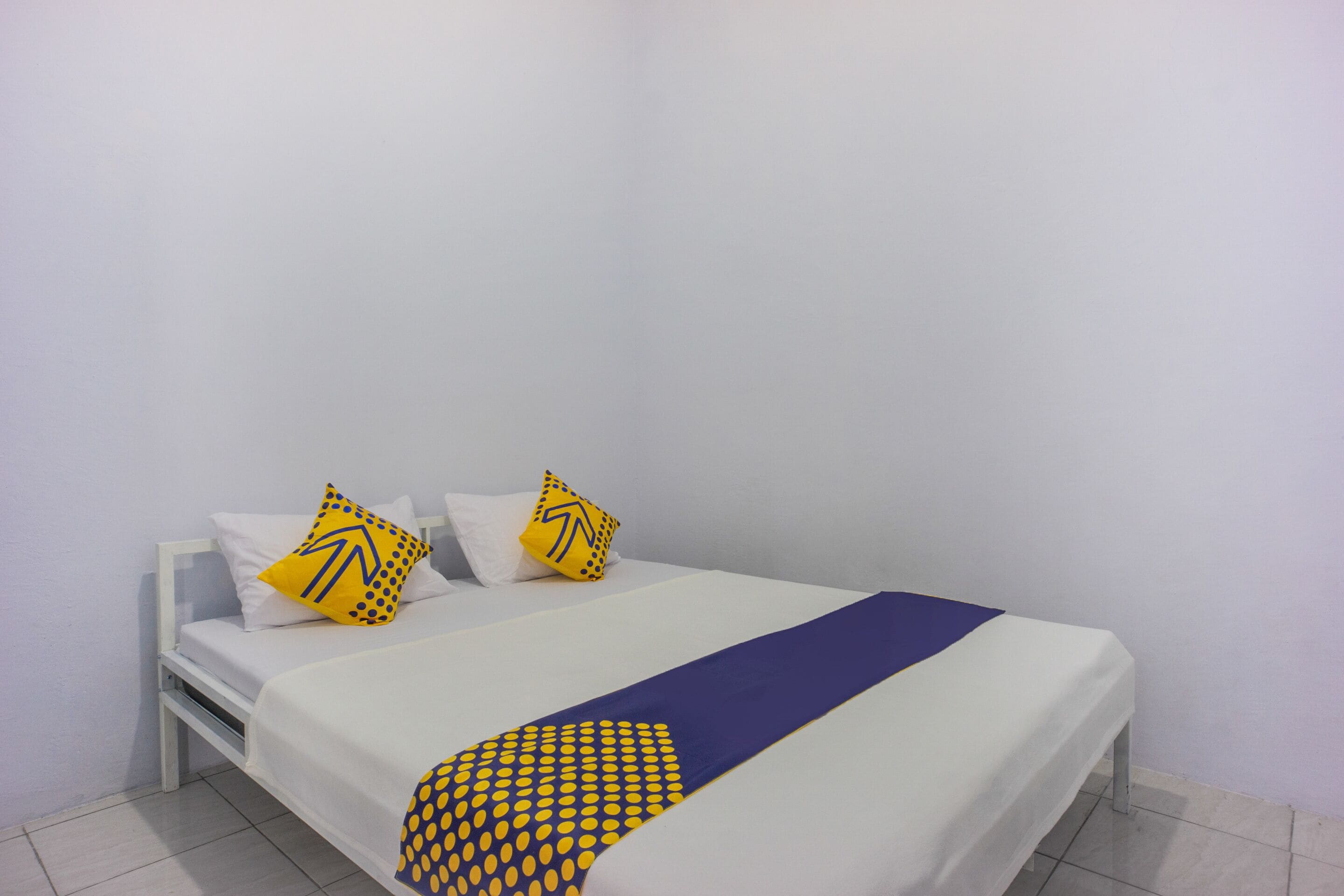 A single bed with white bedding and two yellow pillows with black patterns.