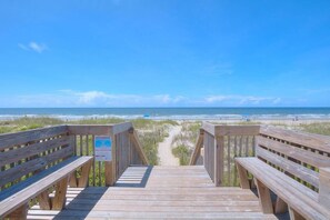 A wooden boardwalk leading to a beach with a clear sky.