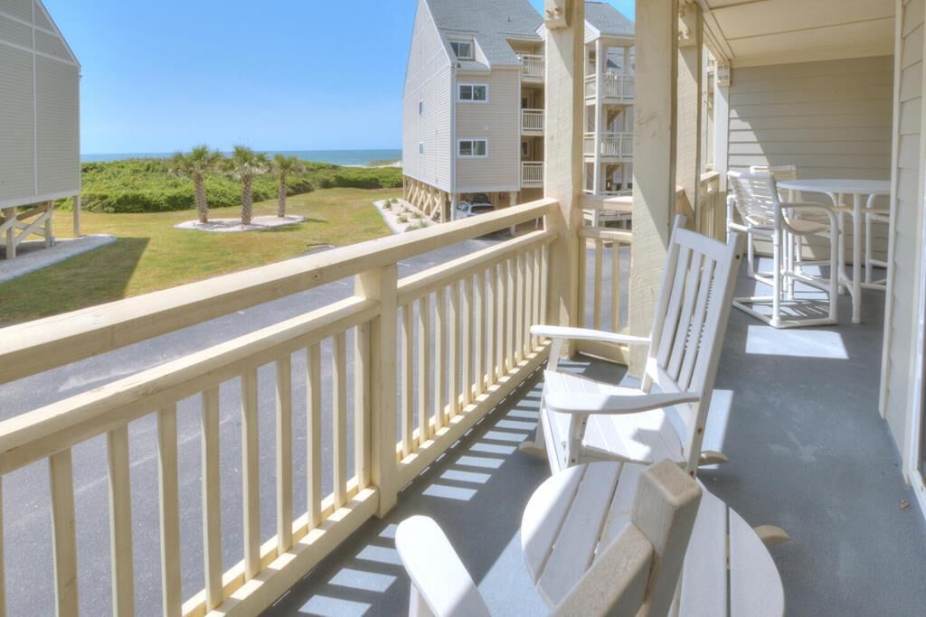 A balcony with white chairs and a table, overlooking a grassy area and buildings.