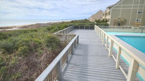 A wooden deck with a pool, overlooking a beach and ocean. - Oceanfront 2BR condo in Caswell Beach, Oak Island—perfect for family getaways! (Oak Island)