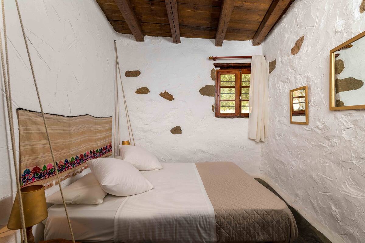 Un dormitorio con cama, ventana y espejo en la pared.