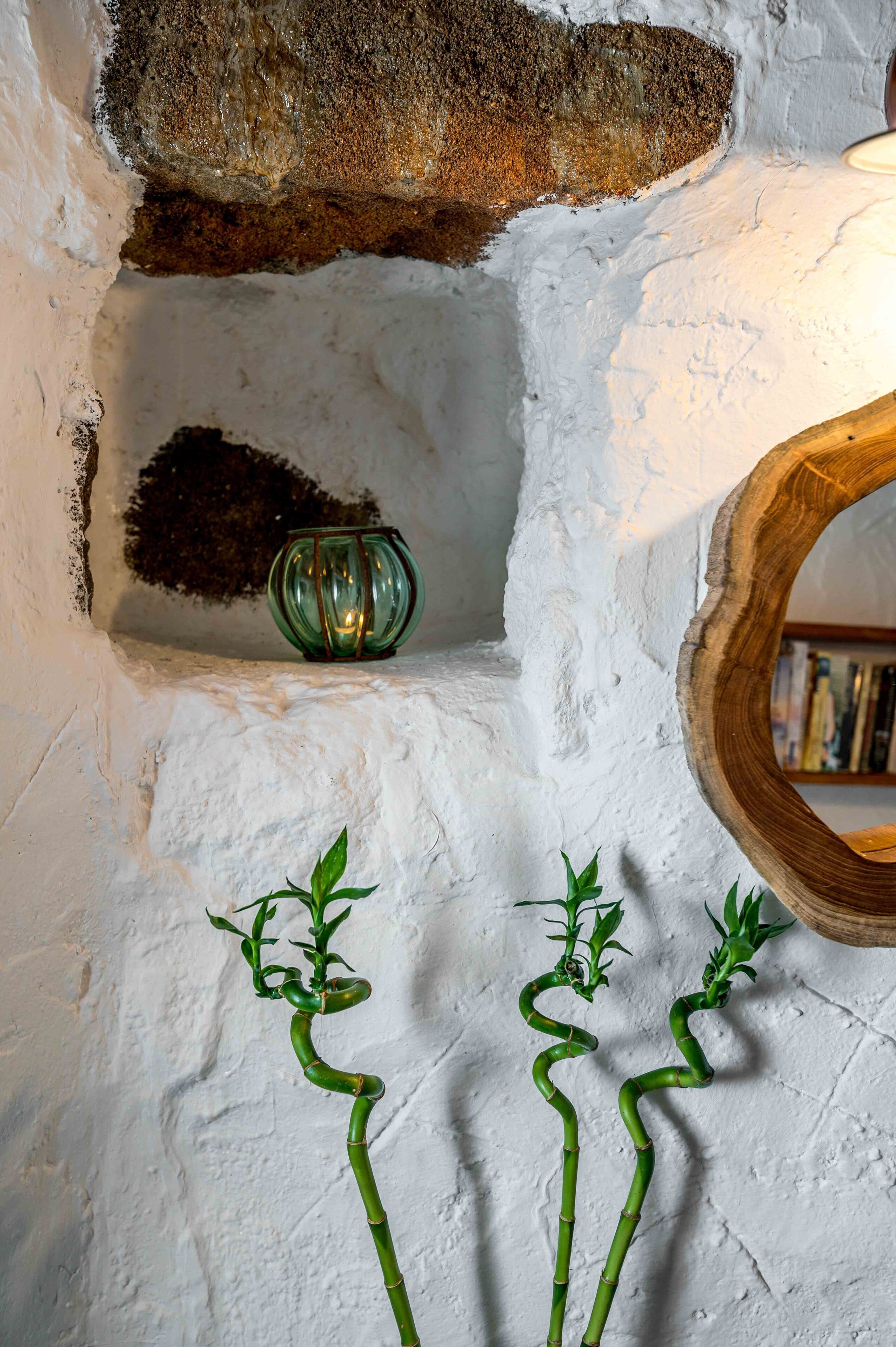 A rustic interior with a stone wall, a wooden shelf, and a green glass vase.