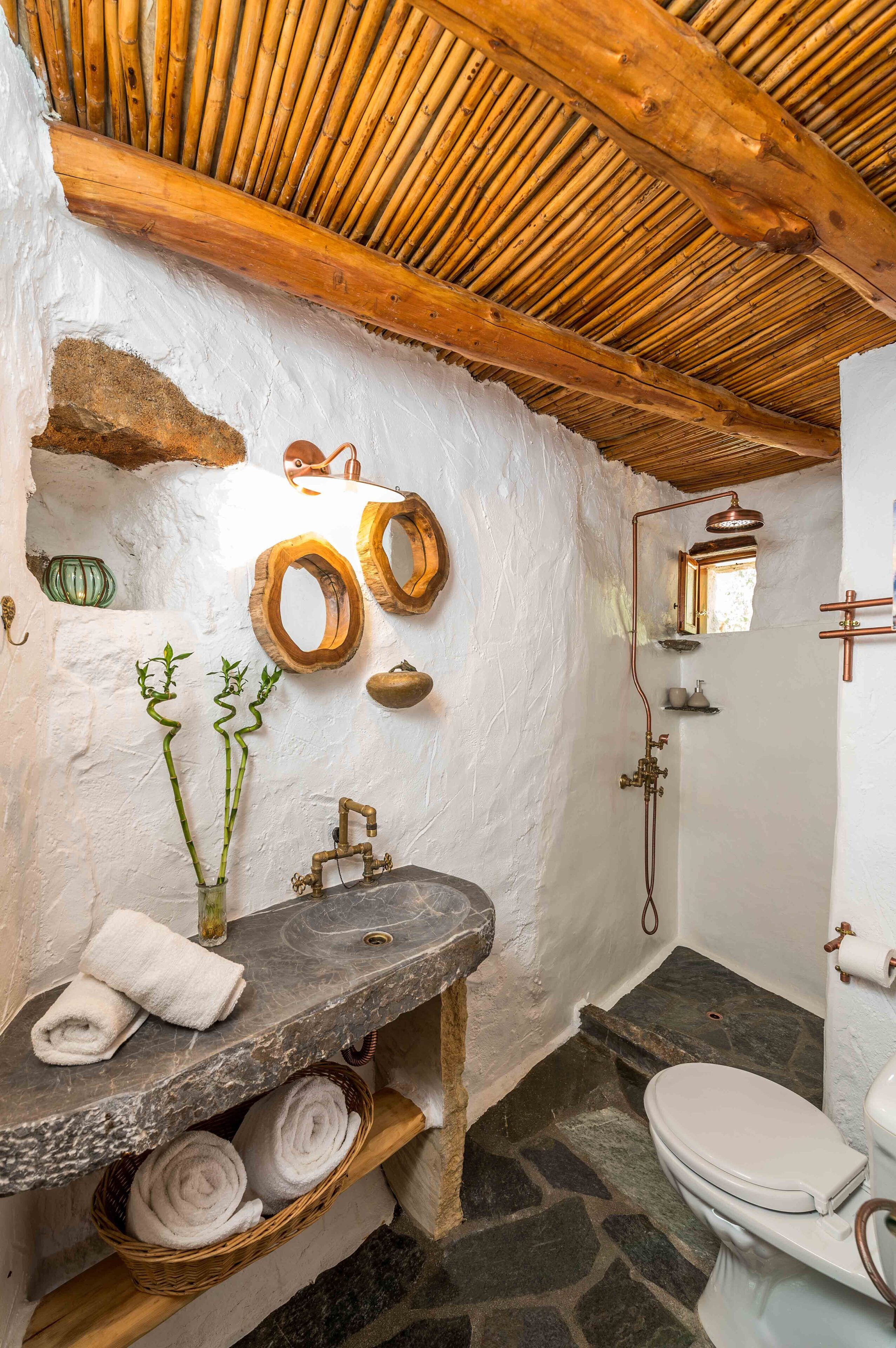 Un baño rústico con lavabo de piedra, vigas de madera y techo de bambú.