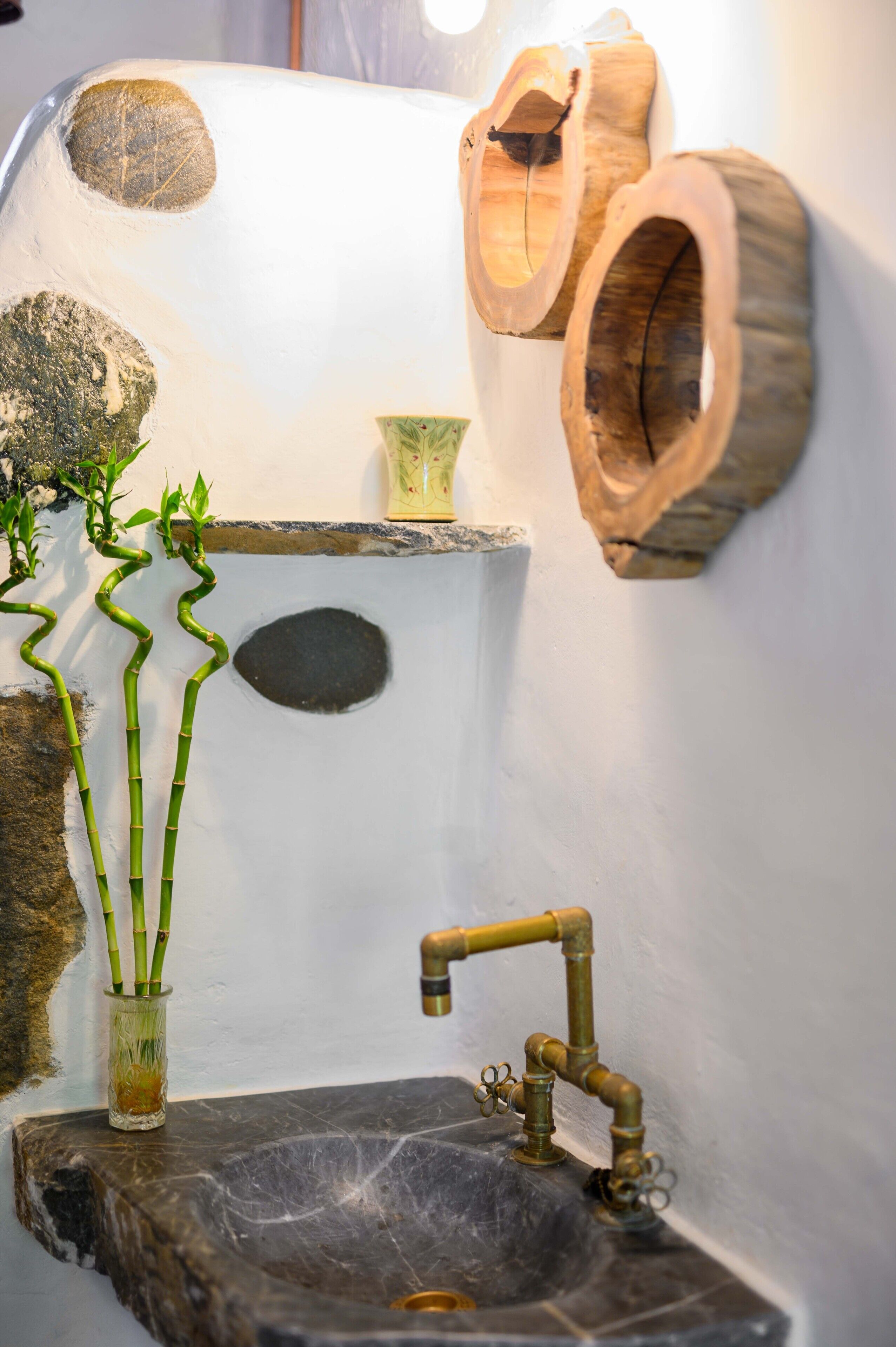 Casa de banho com lavatório de pedra, plantas de bambu e decoração de parede em madeira.