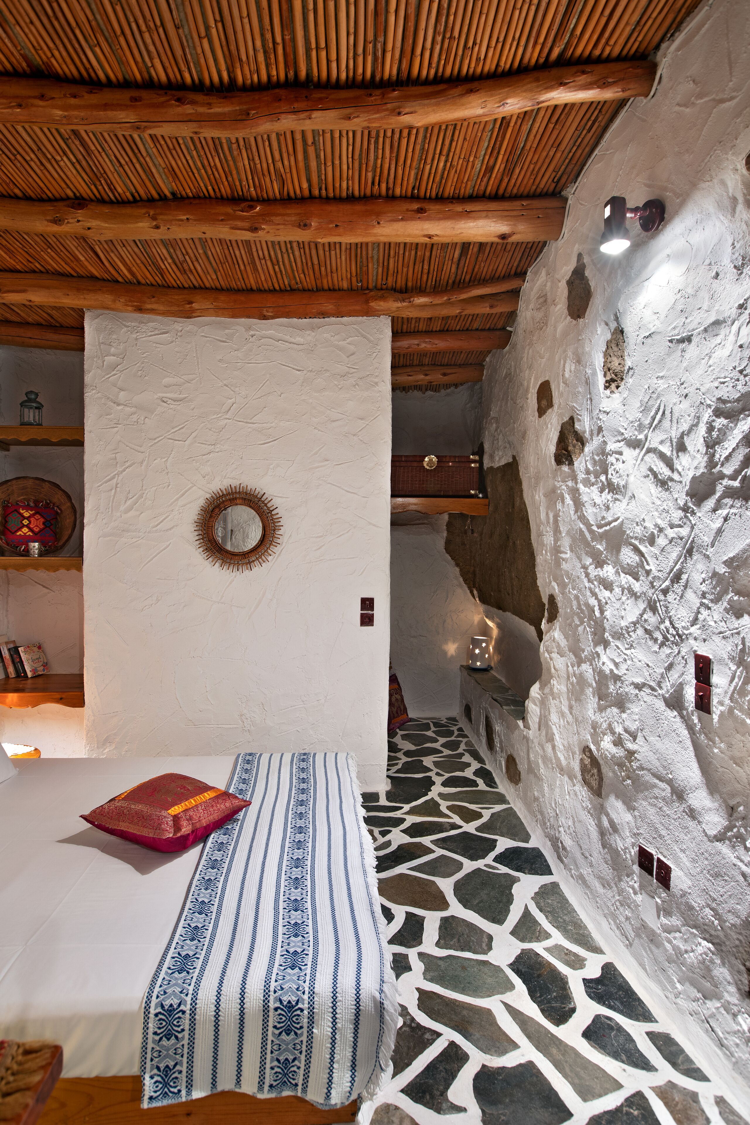 Una habitación con una cama, techo de madera, pared de piedra y un espejo en la pared.