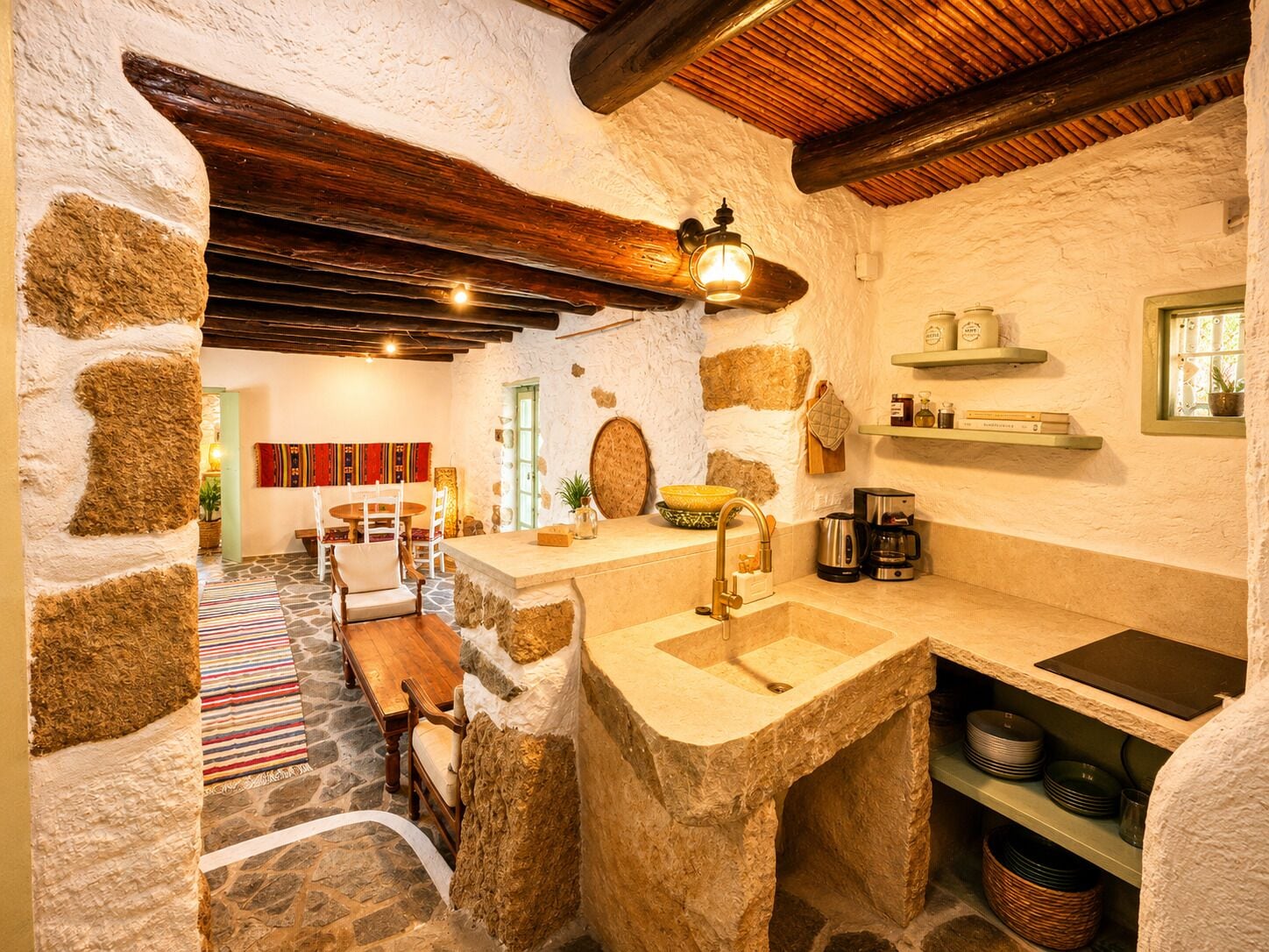 A rustic kitchen with stone walls, a wooden table, and a stone sink.