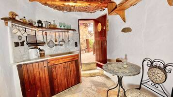 A rustic kitchen with wooden cabinets, a stone floor, and a small dining area with a metal table and chairs.