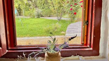 A window with a view of a garden, a potted plant on a window sill, and a striped fabric below the window.
