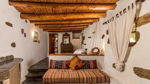 A rustic interior with a wooden ceiling, stone walls, a bench with colorful cushions, and a stone table with pottery. - Natura cottages (Sitia)