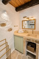 A bathroom with a stone sink, a mirror with lights, a towel rack, and a wooden ceiling.