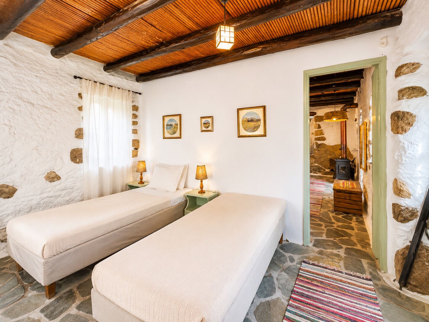 A room with two beds, stone walls, a wooden ceiling, and a stone floor.