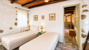 A room with two beds, stone walls, a wooden ceiling, and a stone floor.