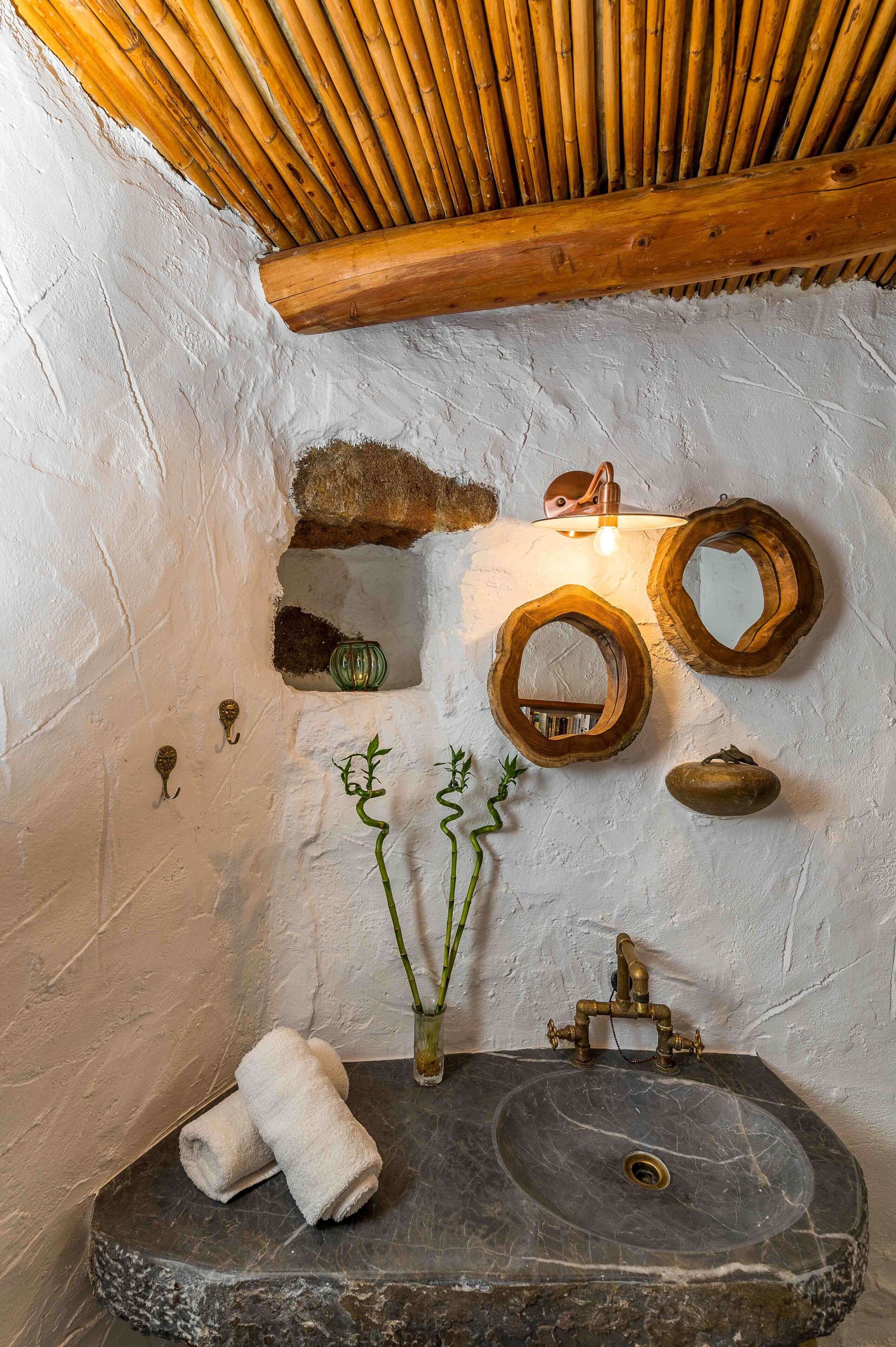 A rustic bathroom with a stone sink, wooden beams, and unique wall-mounted mirrors.
