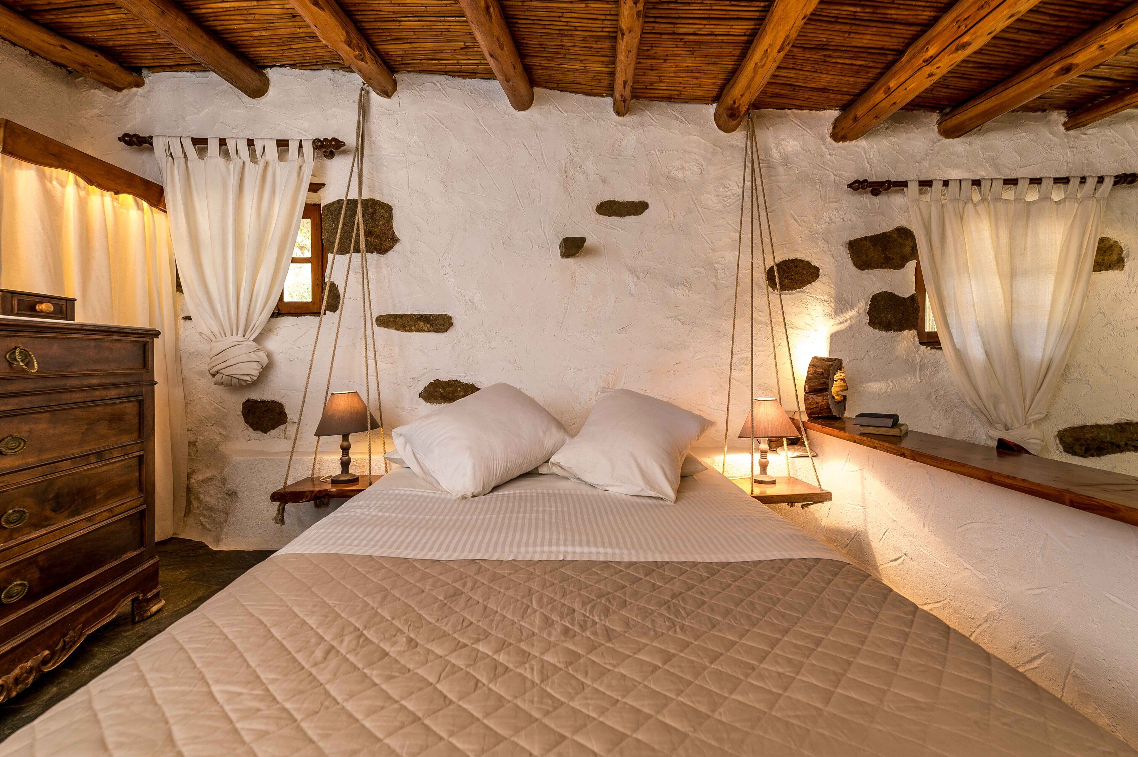 A bedroom with a large bed, wooden headboard, stone wall accents, and a dresser with drawers.