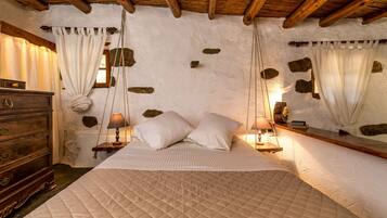 A bedroom with a large bed, wooden headboard, stone wall accents, and a dresser with drawers.