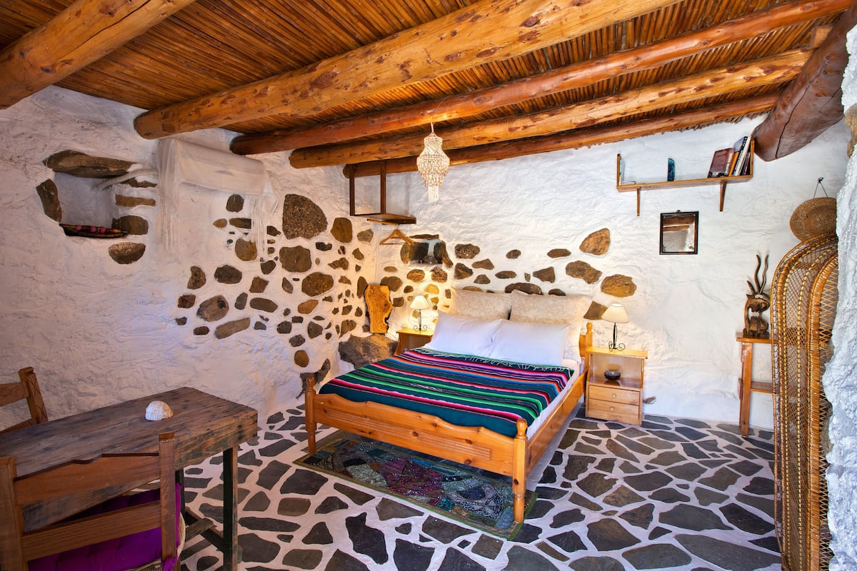 Un dormitorio rústico con suelo de piedra, cama de madera y una mesa de madera.