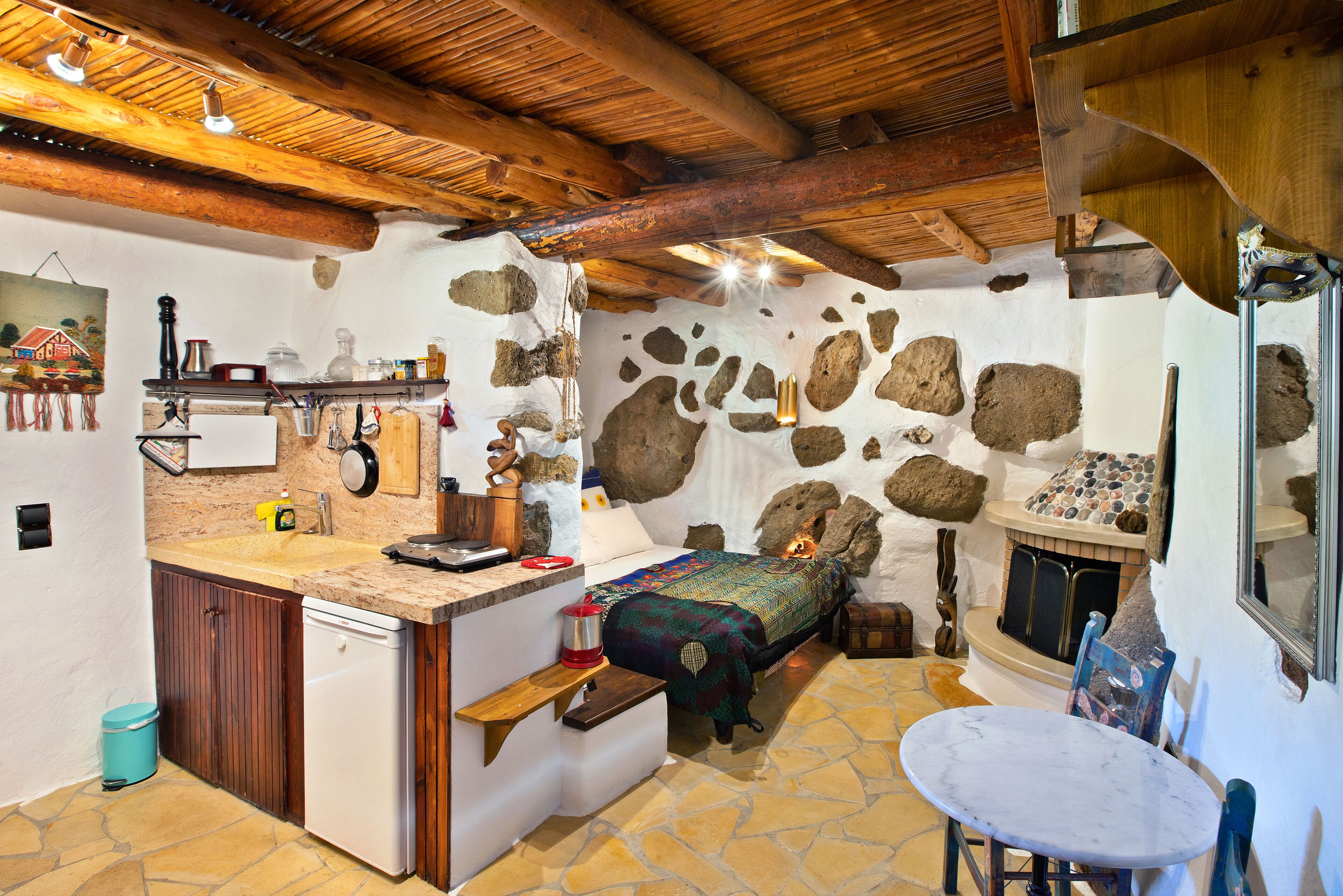 Una camera rustica con parete in pietra, travi in legno, un letto, un tavolino e un camino.