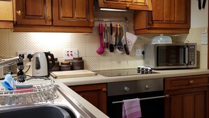 A kitchen with wooden cabinets, a microwave, a kettle, and various utensils hanging on the wall.