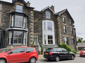 A stone building with a bay window and a black car parked in front. - Lyndale Apartment (Windermere)