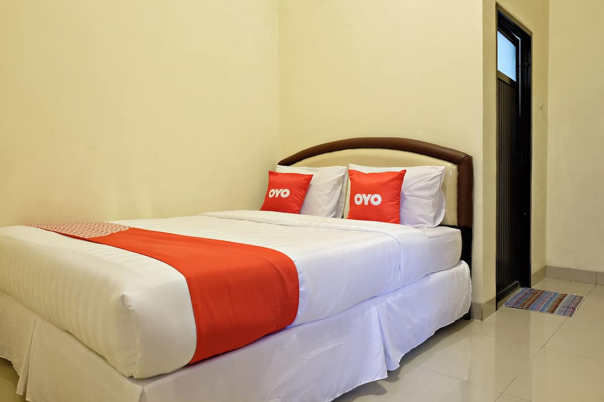 Un lit bien fait, avec une literie blanche et orange, deux oreillers portant le logo « OYO », et une porte sur la droite.