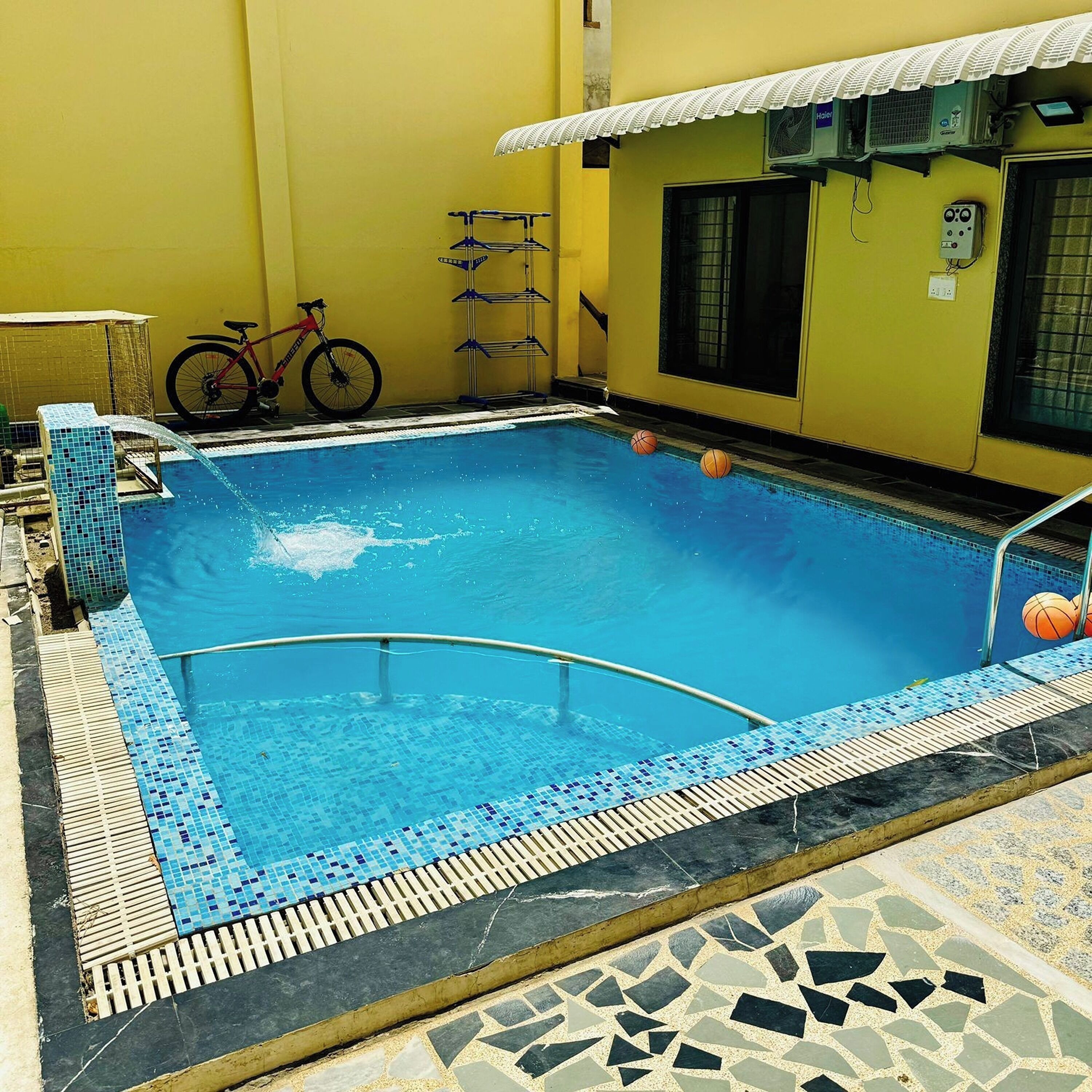 A swimming pool with a tiled edge, a bicycle, and a building with a yellow wall and a window.