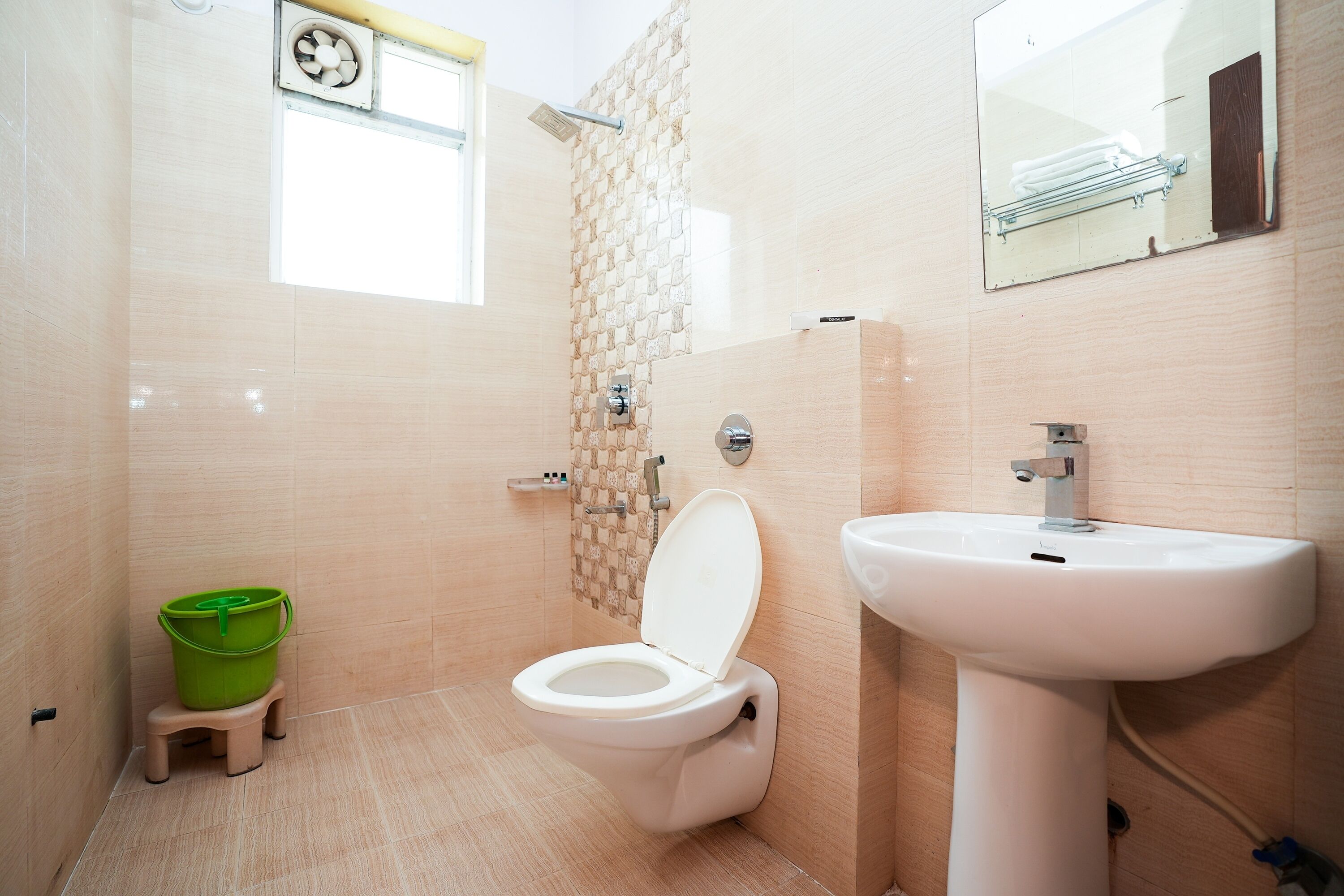 A bathroom with a toilet, sink, and green bucket on a stool.