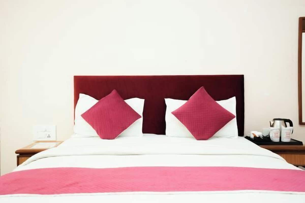A bed with a red headboard, two pillows, a white bedspread, and a pink blanket.